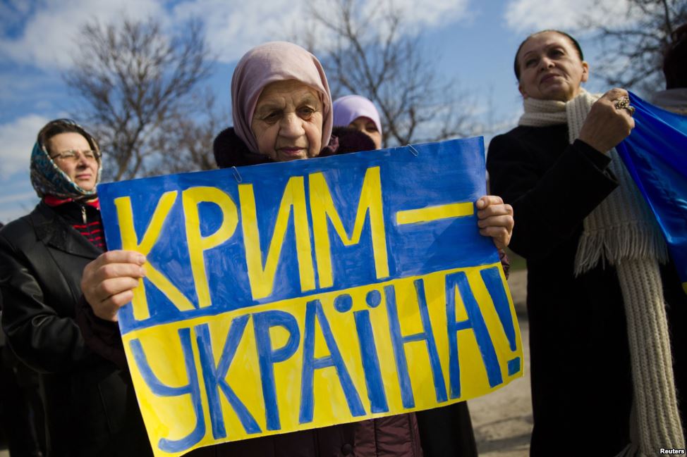A Crimean Tatar woman holds a sign "Crimea Is Ukraine" in protest to the fake "referendum" imposed by force by Moscow in March 2014.