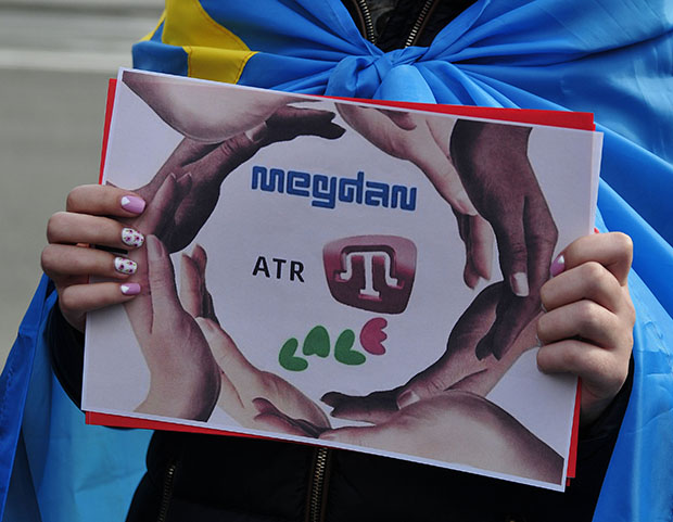 A protester in Europe wearing a Crimean Tatar flag with a sign protesting the shuttering of Crimean Tatar media outlets by Russian occupiers in April 2015 (Photo: Olexei Ivanov, day.kiev.ua)