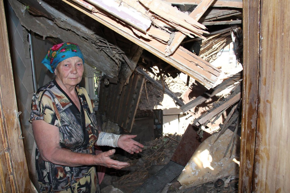 A wounded resident of the Ukrainian town of Maryinka showing her house destroyed as a result of the tank attack and bombardment by Russian heavy artillery and multiple launch missile systems in violation of Minsk-2 Accords, June 2015 (Image: 112.ua)