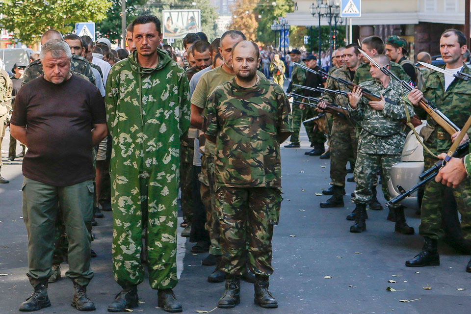 Russian forces (R) armed with assault rifles with bayonets escort a column of Ukrainian prisoners of war during a military parade across central Donetsk on August 24, 2014. Parading POWs this way is a violation of the Geneva Convention. (Image: Maxim Shemetov, REUTERS)