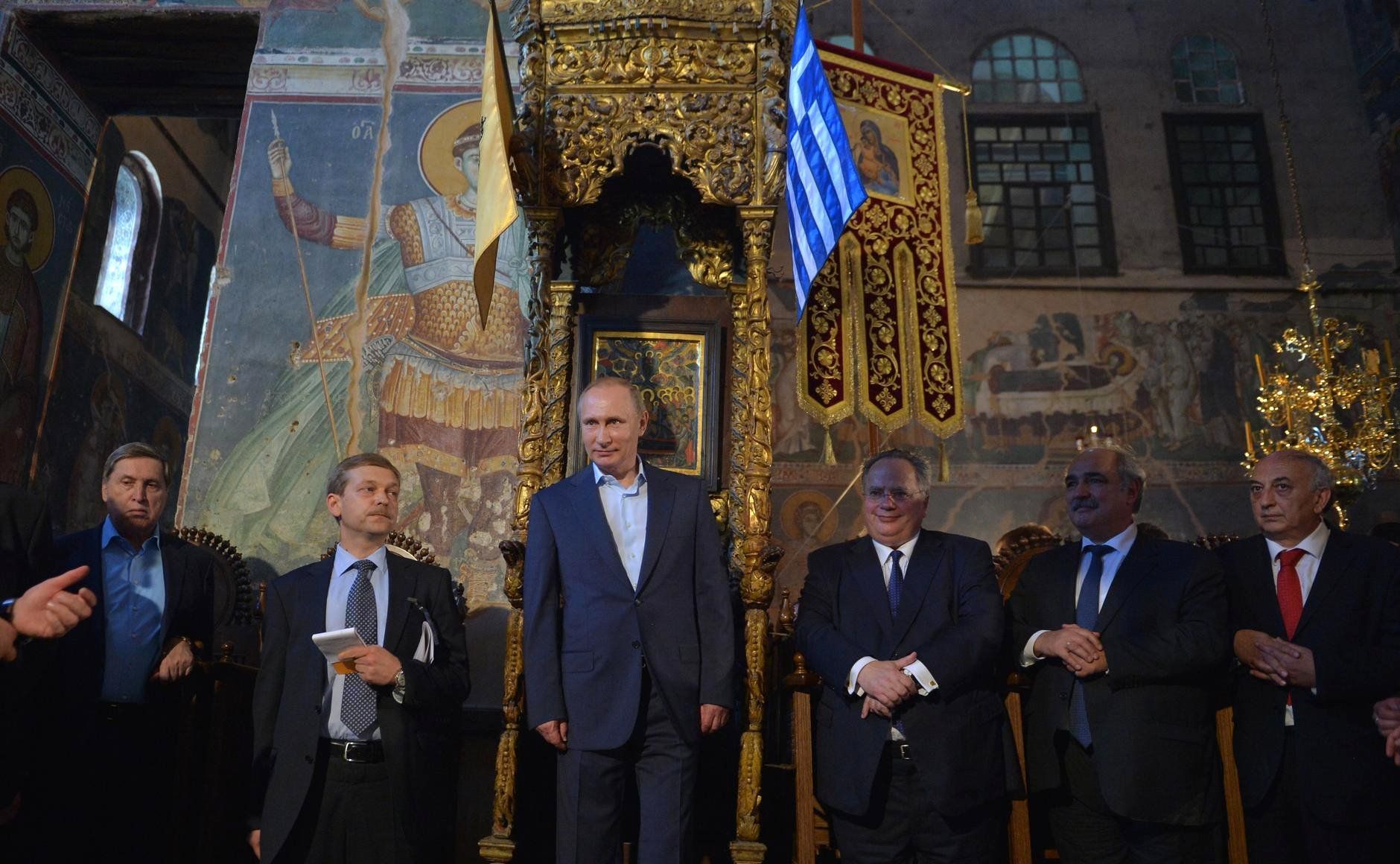 Vladimir Putin visiting Karyes, the Orthodox enclave of Mount Athos. The above photo, of Putin standing at an ancient throne alongside Greek officials and Orthodox dignitaries, was described by various Russian news outlets, both within the country and abroad, as Putin standing at a place which had until now been reserved only for Byzantine emperors. (Image: life.ru)