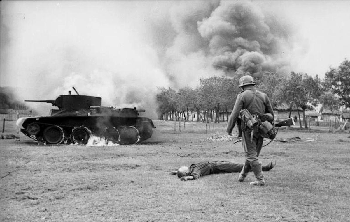 A German infantryman walks toward the body of a killed Soviet soldier and a burning BT-7 light tank in Ukraine in 1941, during the early days of Operation Barbarossa. (Image: Deutsches Bundesarchiv/German Federal Archive)