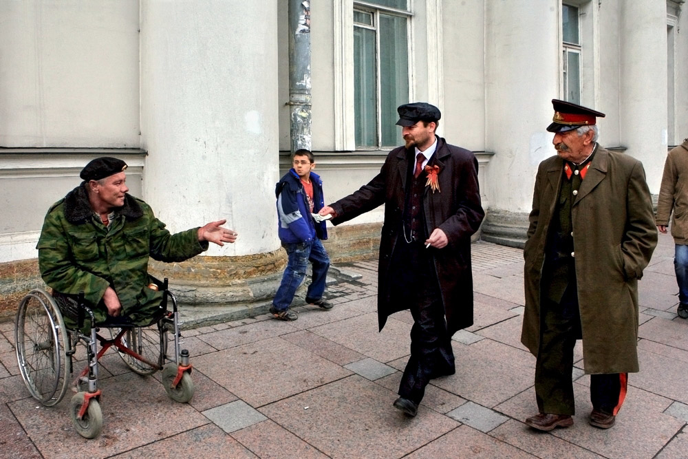 A street scene in St. Petersburg, Russia, the city where Vladimir Lenin's group launched the Bolshevik coupe d'etat of 1917. Lenin and Stalin impersonators giving money to a beggar maimed in one of Putin's wars. (Image: Alexander Petrosyan)