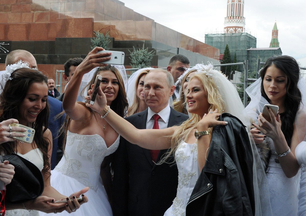 Vladimir Putin at a staged photo shoot with models posing as brides, which was later presented to Russian and foreign media as Putin's random encounter with a group of real brides who charmed him to take some "selfies" while encircled by bodyguards. Red Square in Moscow, September 2016 (Image: TASS)