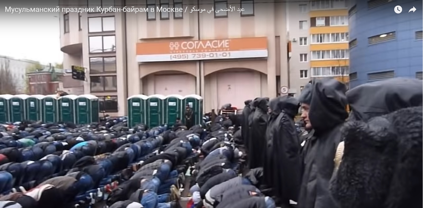 A collective prayer during the Kurban Bayramı Muslim festival in Moscow. Due to the dire shortage of mosques in the city, the faithful pray under the rain in the street while Russian policemen in black rain coats watch over them. (Image: video capture)