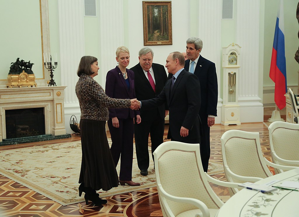 With U.S. Secretary of State John Kerry looking on, Russian President Vladimir Putin greets Assistant Secretary of State for European and Eurasian Affairs Victoria Nuland before the Secretary's meeting with the Russian President at the Kremlin in Moscow, Russia, on December 15, 2015. [State Department photo/ Public Domain]