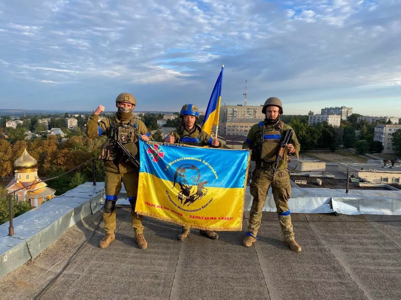 Soldiers of the 1st battalion of Ukraine’s 92nd brigade holding the Ukrainian flag on the rooftop of the city council of Kupiansk, Kharkiv oblast. 10 September 2022. Source. ~