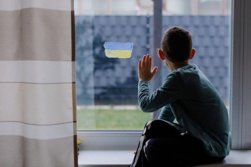 boy looks outside window ukrainian flag