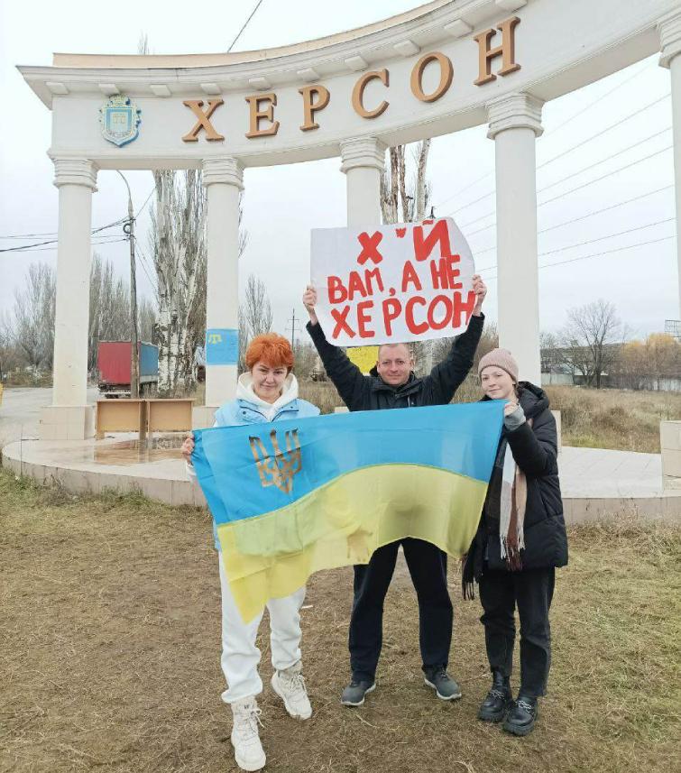 The Kolesov family holds a placard that reads, “Get f*cked and get out of Kherson.”
